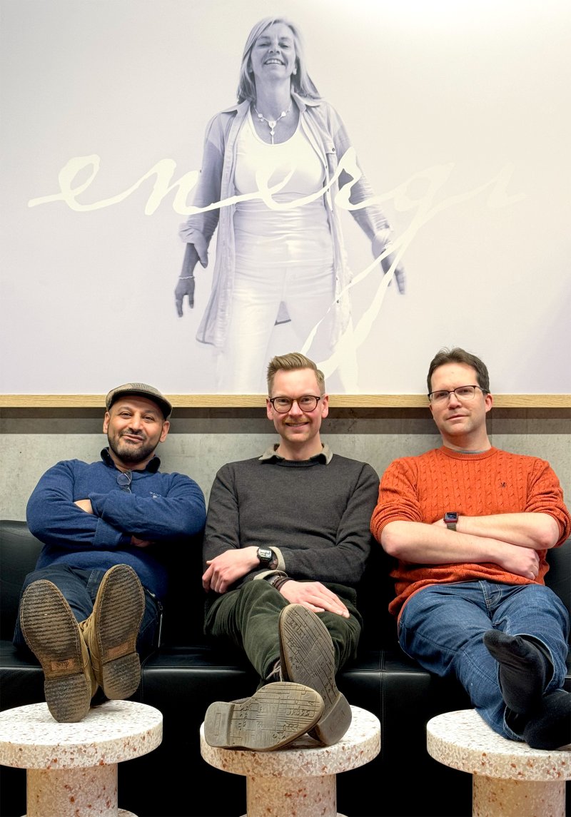 Tre smilende mannlige nyansatte som sitter i en sofa