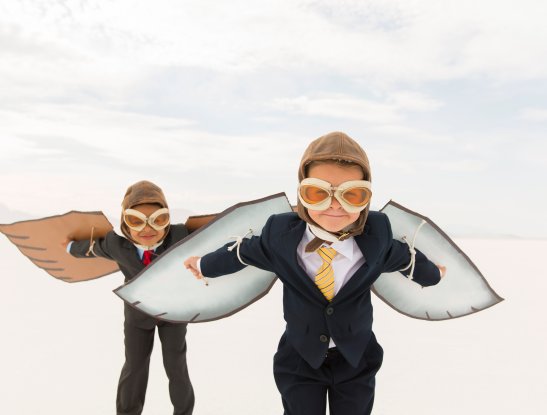 Close up of two young business boys dressed in business suits wearing cardboard bird wings and aviator goggles. They are ready to fly their business into the sky. The boys are standing on the surreal Bonneville Salt Flats in Utah, USA.